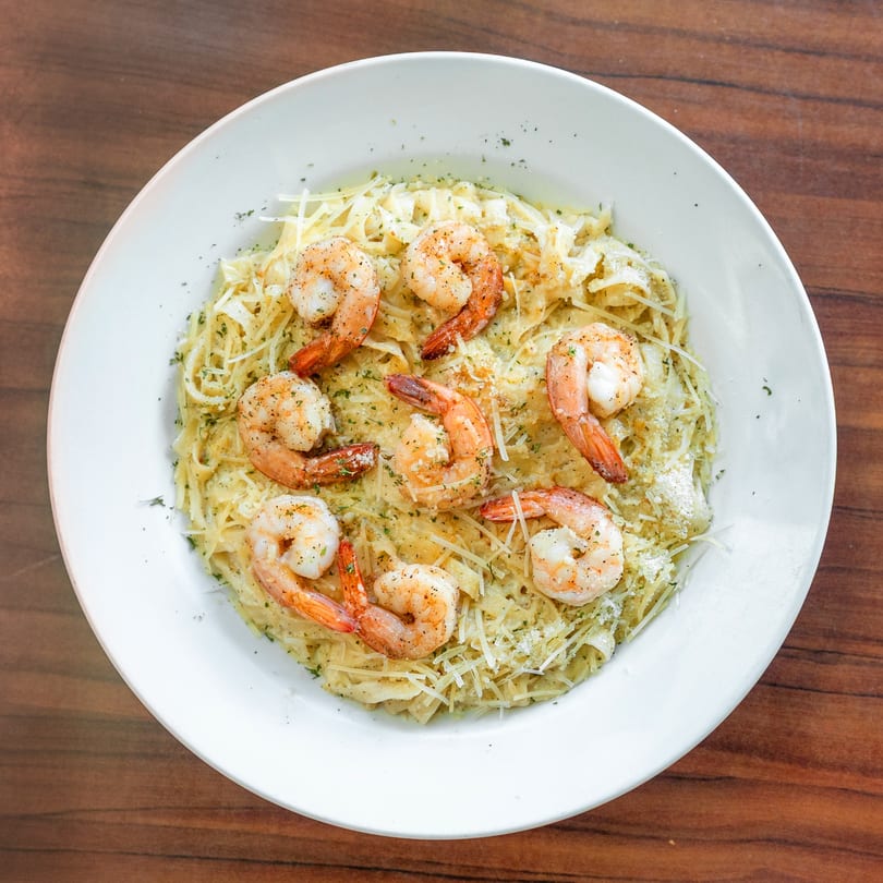 Shrimp pasta dish with parmesan cheese and herbs in a white bowl on a wooden table.