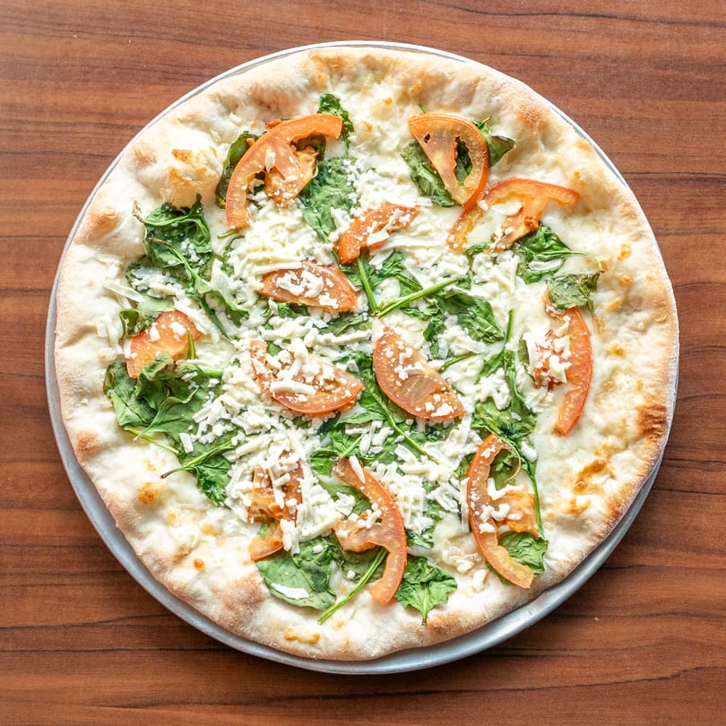 Newyork Pizza Macedonia's white pizza with spinach, sliced tomatoes, and shredded cheese.