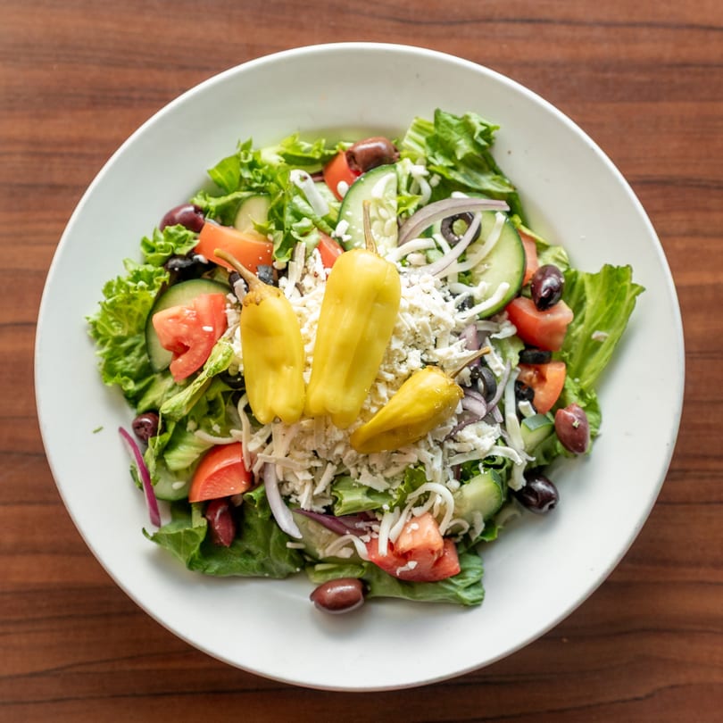Fresh Greek salad with lettuce, tomatoes, cucumbers, olives, feta cheese, and yellow peppers.