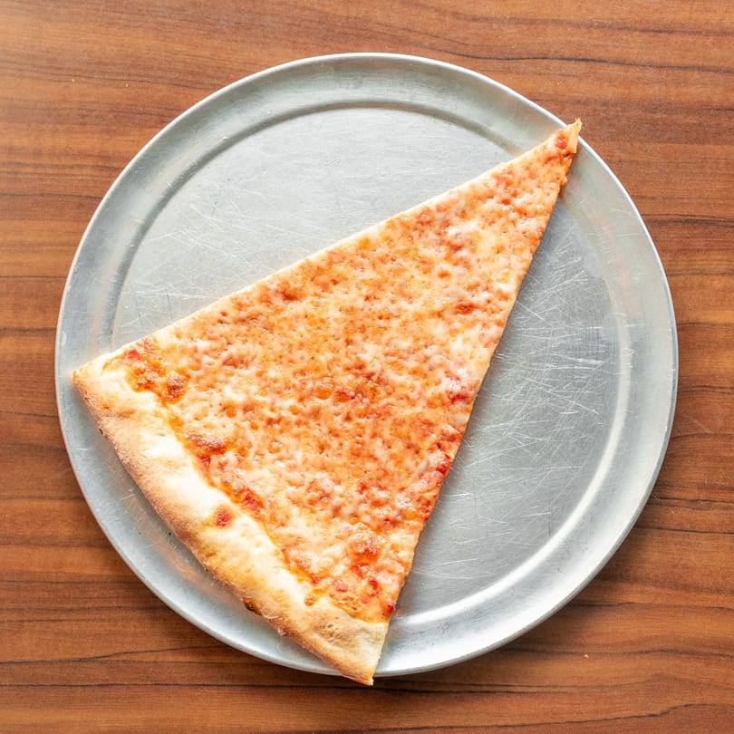 A single slice of New York-style cheese pizza on a metal pan, centered on a wooden table.