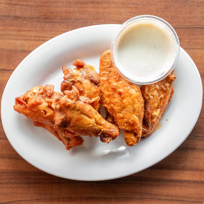 Four crispy, golden-brown chicken wings with a side of creamy dipping sauce on a white plate.