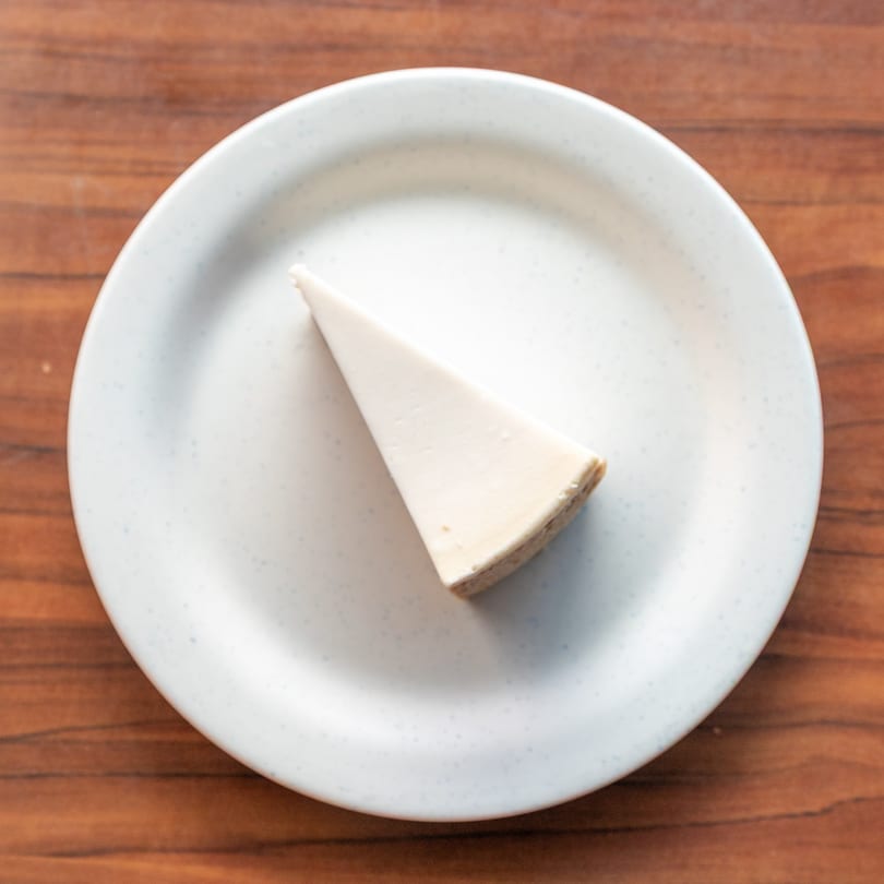 A slice of plain cheesecake with a graham cracker crust on a white plate.