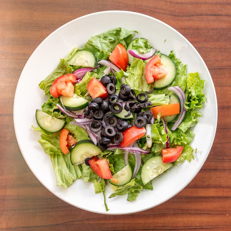 Fresh garden salad with lettuce, tomatoes, cucumbers, red onions, and black olives in a white bowl.
