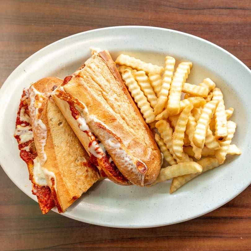 Two toasted meatball subs with melted cheese and marinara sauce, served with crinkle-cut fries.