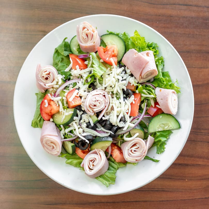 Fresh salad with lettuce, tomatoes, cucumbers, olives, shredded cheese, and rolled deli meat.