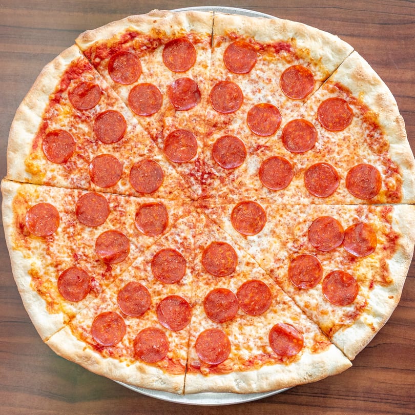 A large, sliced Newyork Pizza Macedonia pepperoni pizza on a metal tray.