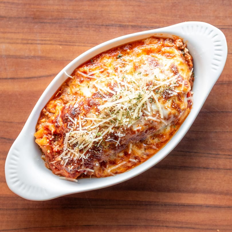 Baked lasagna with melted cheese and herbs in a white oval dish on a wooden table.
